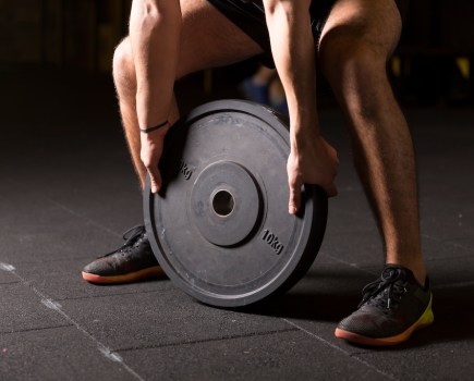 Caucasian muscular man exercising by the use weight plate in the gym. Dark photography concept with copy space.