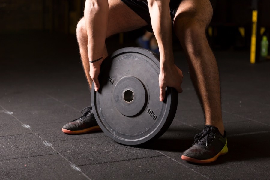 Caucasian muscular man exercising by the use weight plate in the gym. Dark photography concept with copy space.