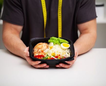 A man holding a container of healthy food with a tape measure round his neck