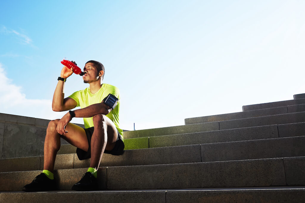 Athletic man sat on outside steps drinking bottle of water