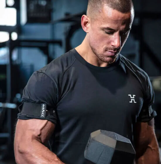 Man in gym lifting dumbbell with HYTRO BFR strap on his arm