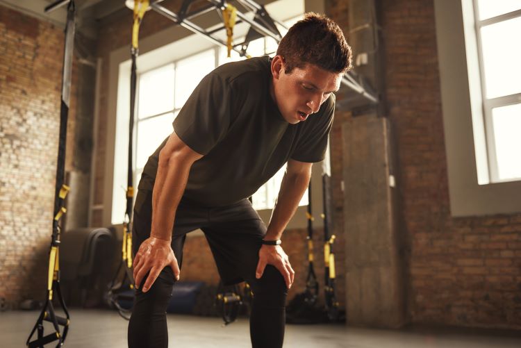 A man in a gym, on his haunches and breathing heavily