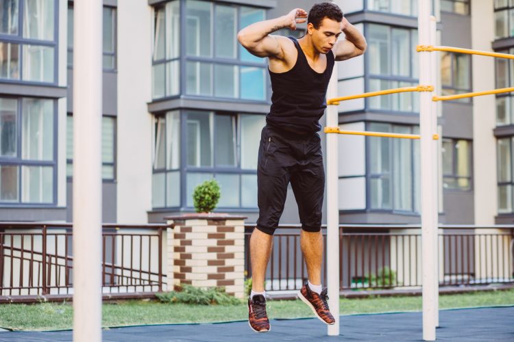 A man in a park jumping up to perform a burpee – one of the best exercises if you want to know how to burn belly fat