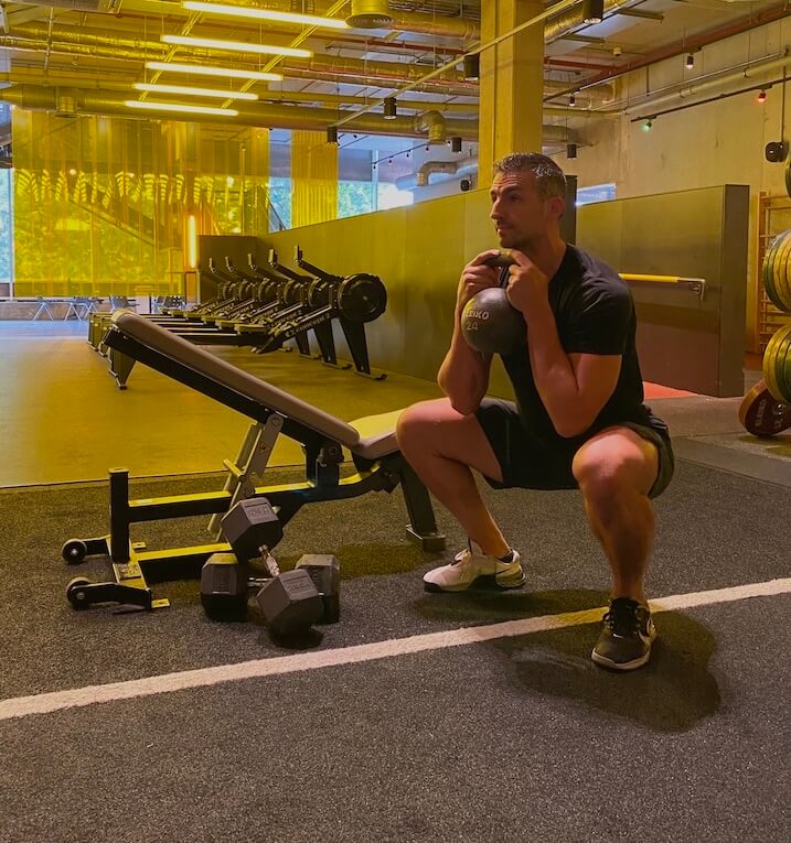 man performing goblet squat with kettlebell