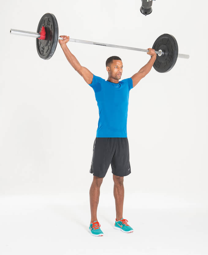 man in blue t-shirt and shorts performing overhead squat with barbell