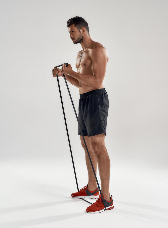 topless man demonstrating how to use resistance bands with a resistance band curl