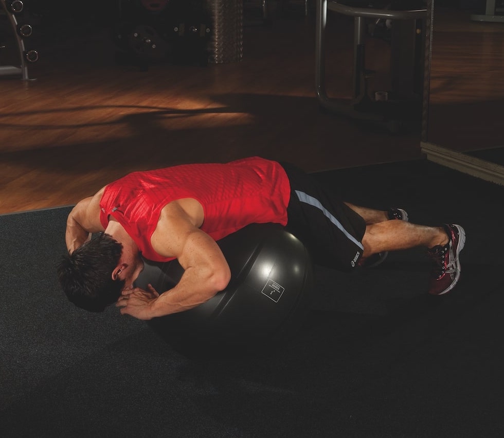 man in red vest and shorts performing the first stage of a Swiss ball back extension