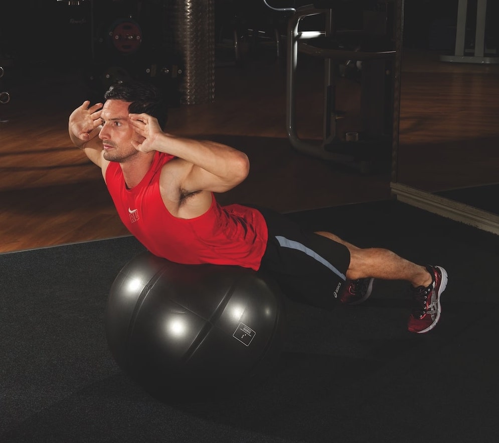 man in red vest and shorts performing the second stage of a Swiss ball back extension