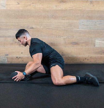 Part of the best full-body dumbbell workout: a man performing a 90 90 hip opener demonstration, sitting with legs at 90 degrees, stretching over front leg