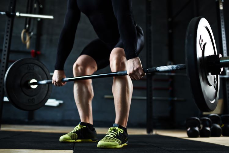 Lower torso of a man lifting a barbell in the gym