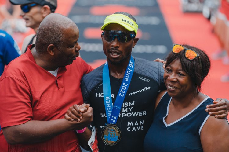 Sam wearing a medal at the finishing line, with his mum and dad