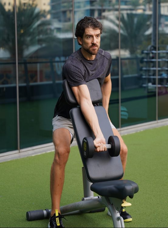 Man using a seat to perform end of dumbbell preacher curl