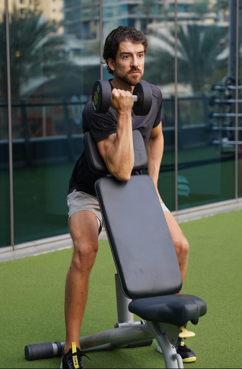 Man using bench to perform start of dumbbell preacher curl
