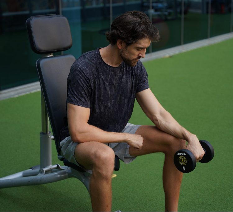Man seated performing start of dumbbell inverted forearm curl
