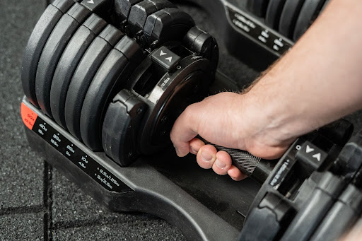Man's hand lifting a Powerhouse Fitness adjustable dumbbell