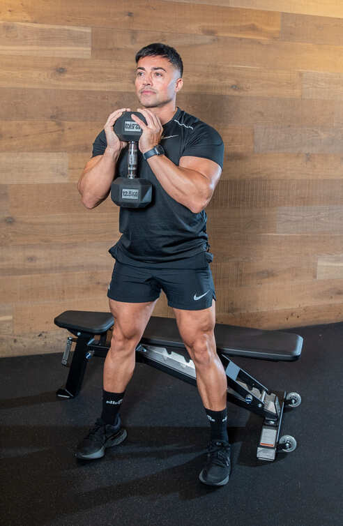 man demonstrates goblet squat - holding a weight in both hands, he stands upright, legs shoulder-width apart