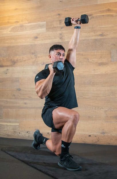 man alternates weight presses overhead in a kneeling position