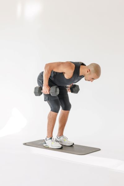 man demonstrating bent over back rows: bent at the hips and learning forwards, he pulls each dumbbell up towards his body