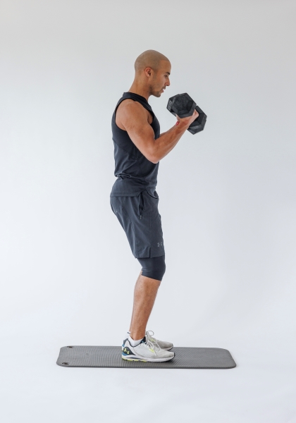 man demonstrates dumbbell bicep curl: standing upright, he holds a dumbbell in each hand before raising and lowering them in a controlled manner