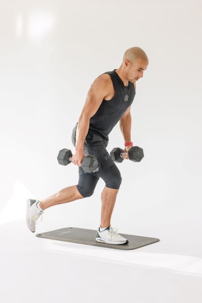 man demonstrates curtsy lunges: holding a dumbell in each hand, he steps one foot behind and across from him