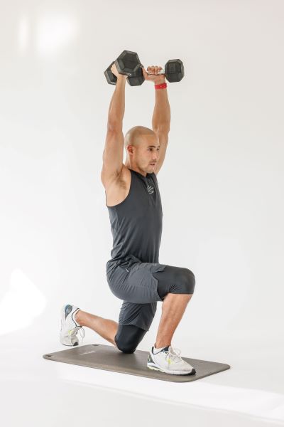 man demonstrating reverse lunge press step 2: he steps back and lunges one leg behind him while pressing the dumbbells overhead