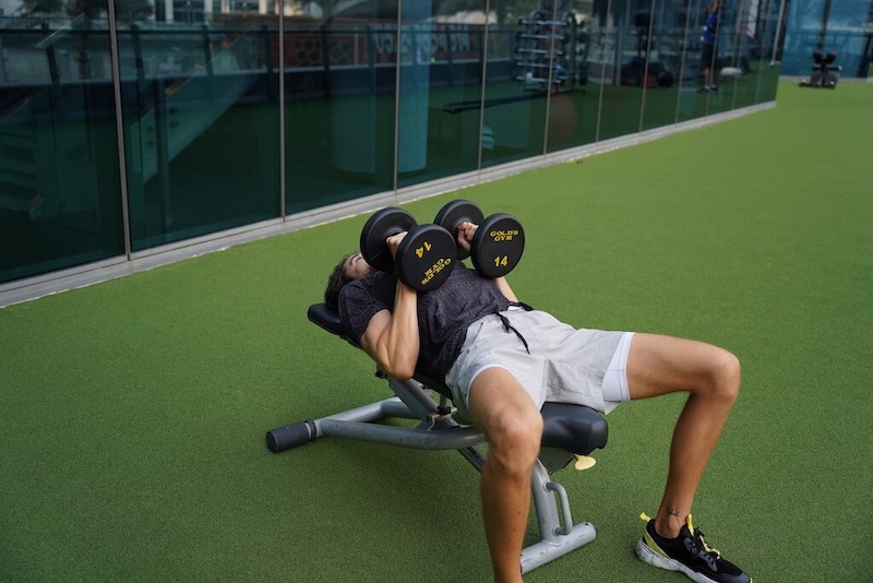 man demonstrating dumbbell triceps press in outdoor gym