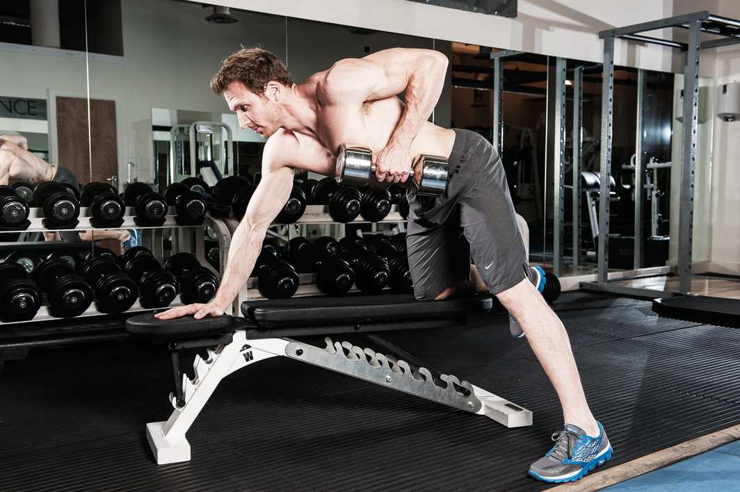 man demonstrates single arm dumbbell row in gym