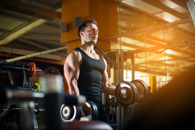 A man in a balck vest lifting dumbbells in a gym - how to get bigger arm muscles