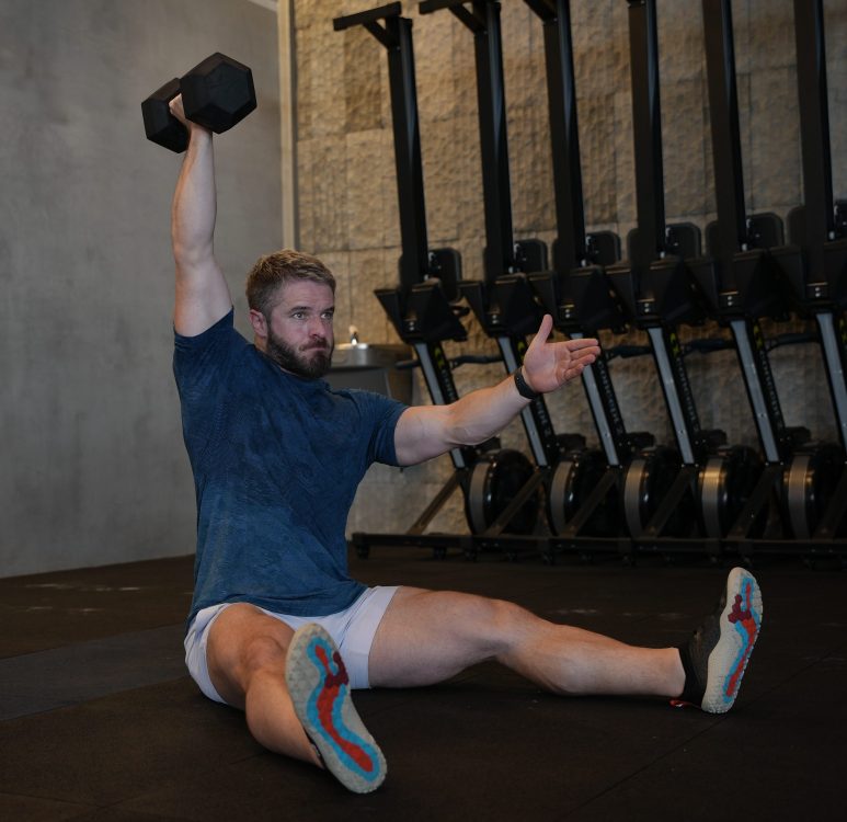 Man performing end of dumbbell floor Z press - best shoulder press variations