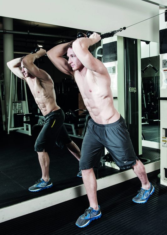 Man performing the standing cable superman - how to build bigger arm muscles