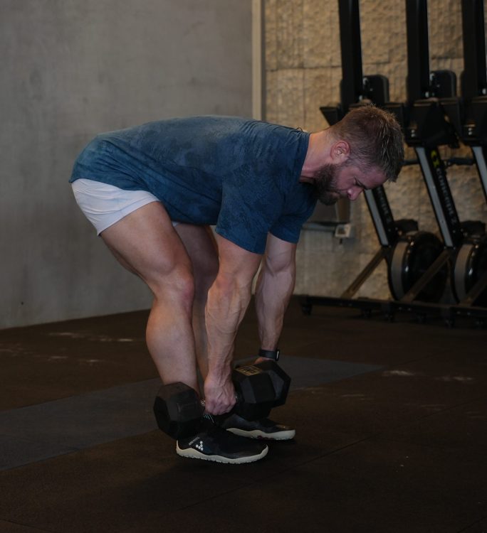 Man performing end of romanian exercise with dumbbells