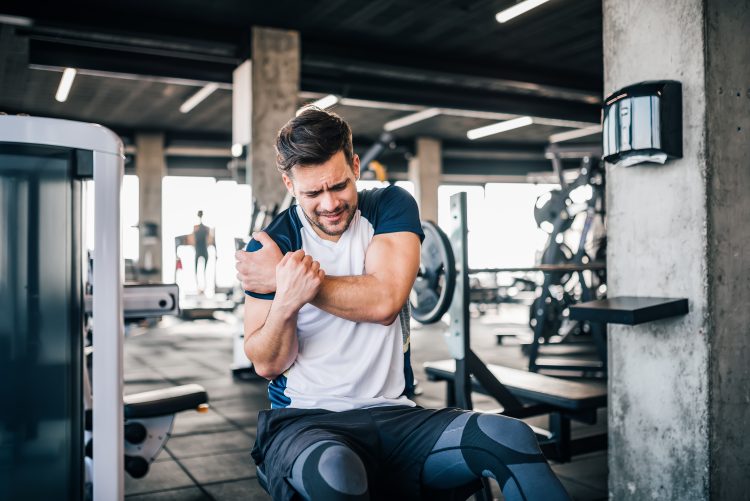 A man clutching his injured shoulder in the gym - get stronger by training less