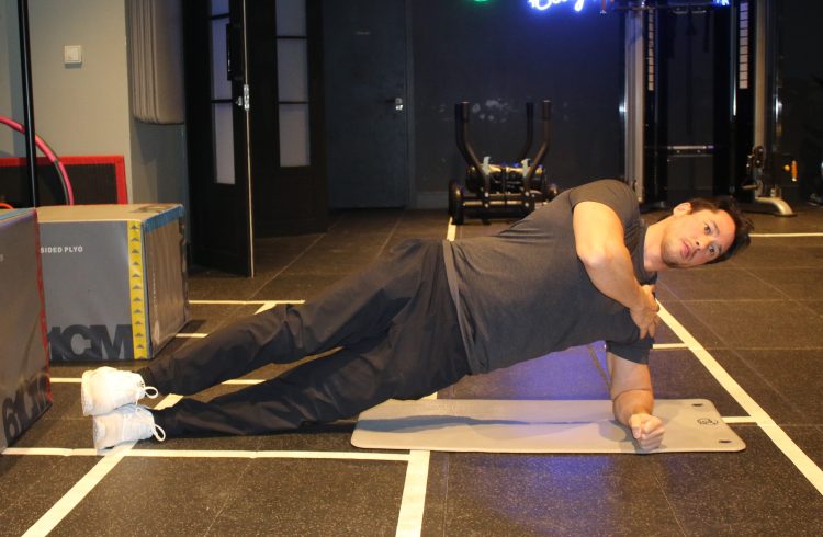 Man in a gym performing a side bridge - best lower back exercises