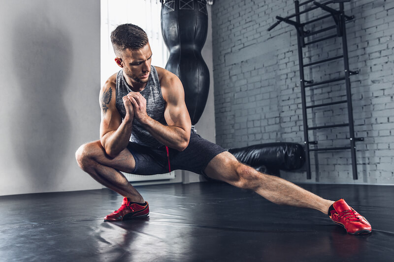 Man in gym stretching his lower body with a lateral lunge