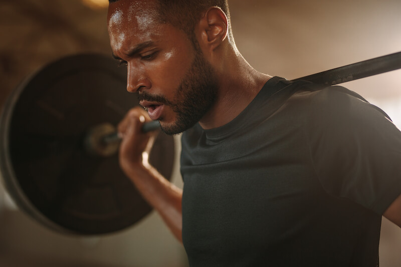 close up of man with barbell on back performing squat 