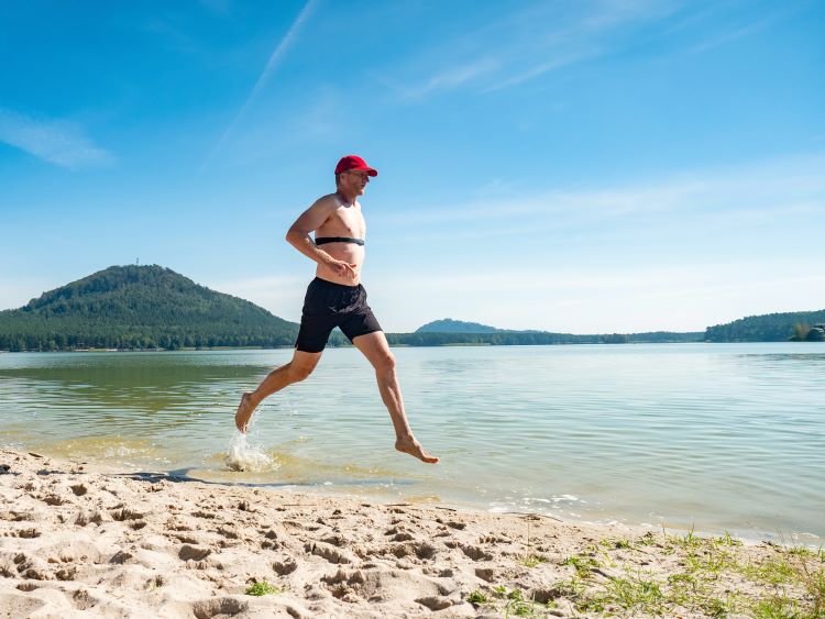 Man running along the sea shore wearing a heart rate monitor