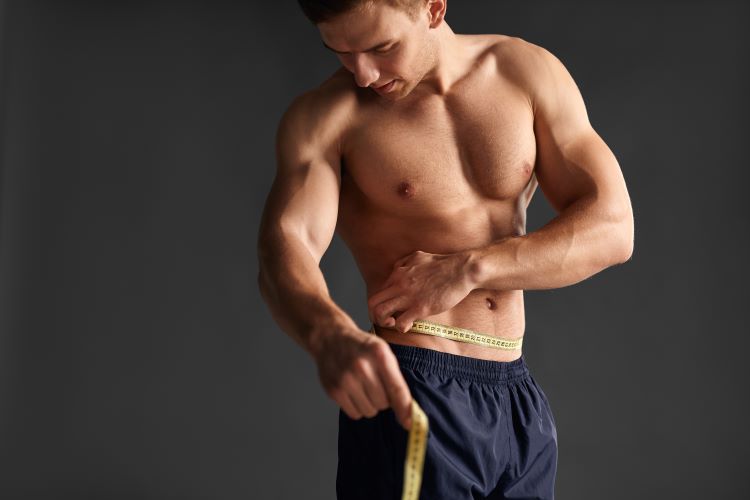 A shirtless man measuring his waist