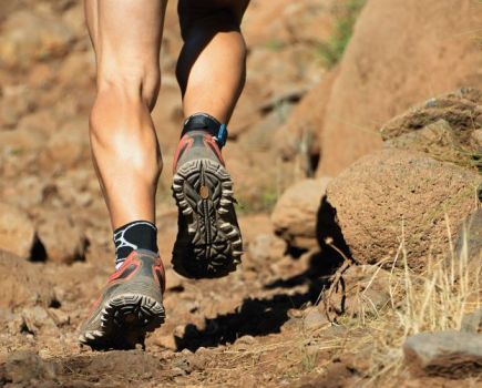 The lower legs of a man running off road, trail shoes vs road shoes concept