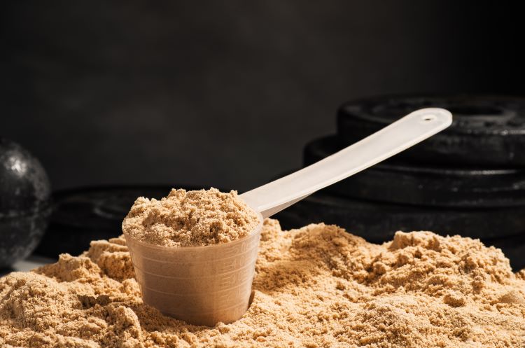 A scoop of protein powder with weights in the background