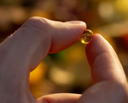 Man's hand holding a vitamin D capsule