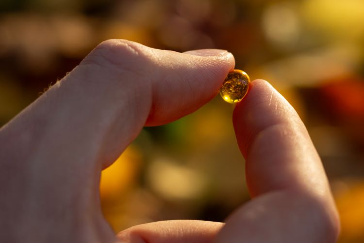Man's hand holding a vitamin D capsule