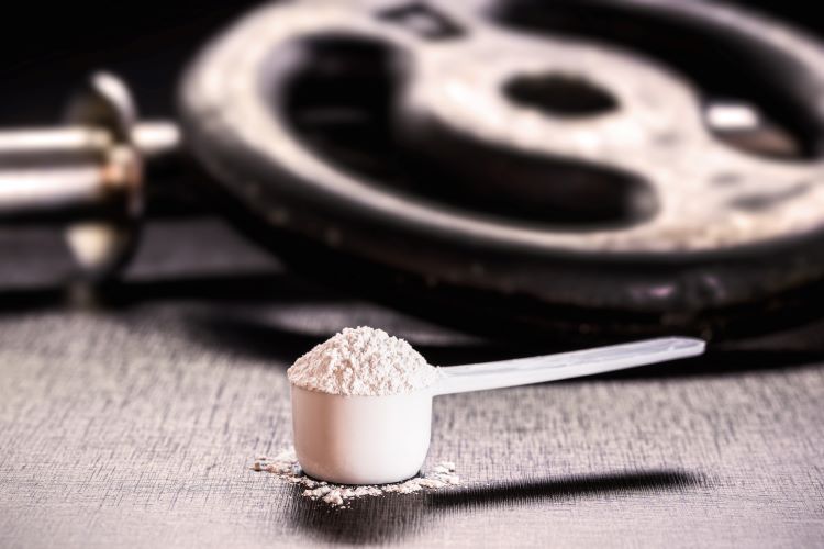 Scoop of creatine powder with weights in the background