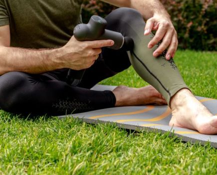 Lower torso of a man using a massage gun on his legs