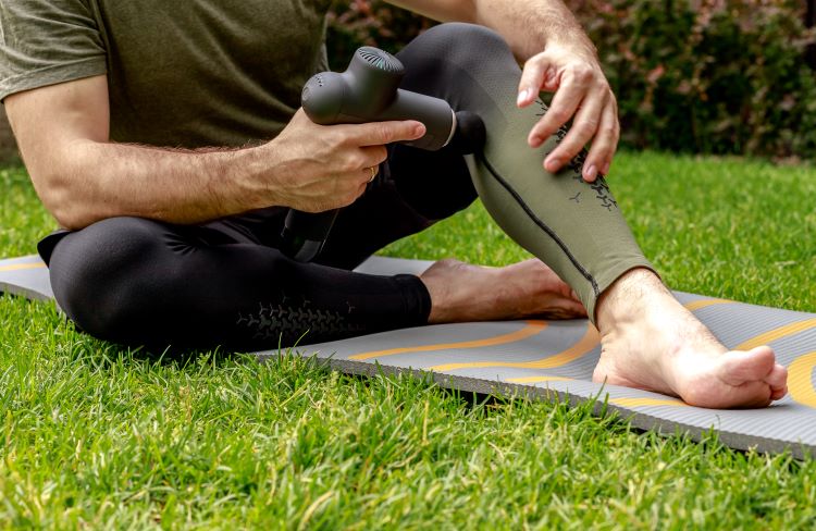 Lower torso of a man using a massage gun on his legs