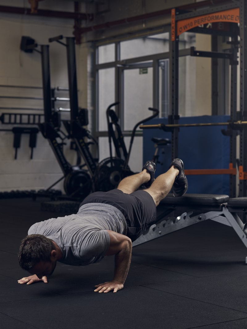 man demonstrates how to do decline press ups using a bench