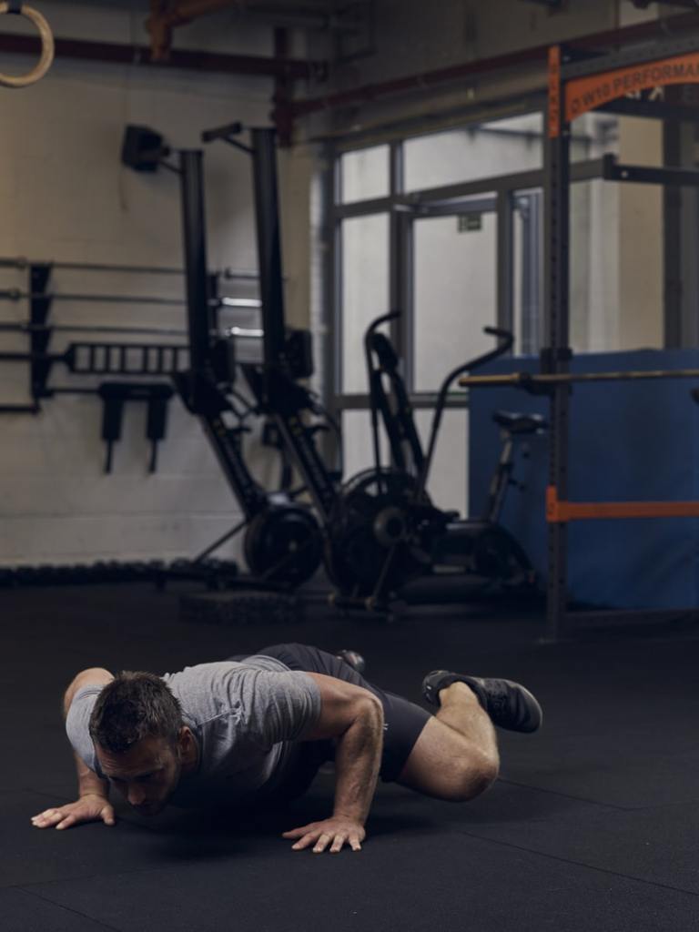 man lowers into spiderman press up while lifting one bent leg, showing best bodyweight exercises to build strength