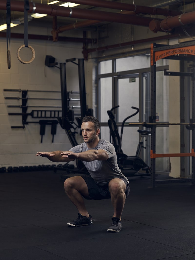 man performs a squat in the gym, one of the best bodyweight exercises