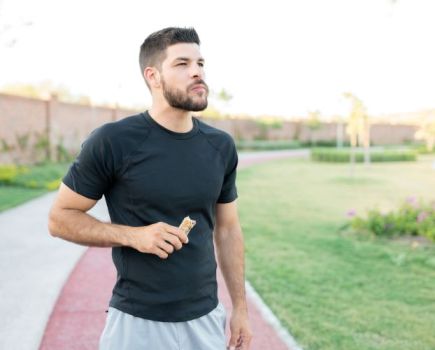 Man by a running track eating a protein bar