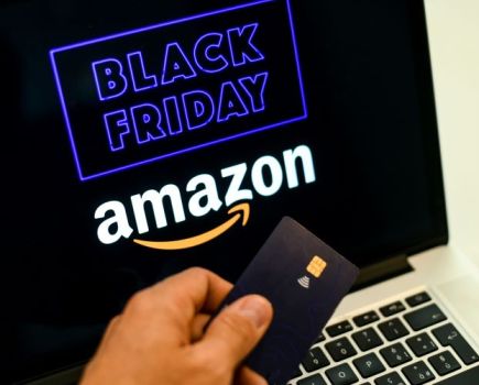 Close up of a man holding a credit card by a laptop screen advertising Black Friday