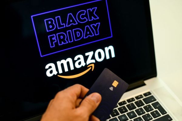 Close up of a man holding a credit card by a laptop screen advertising Black Friday